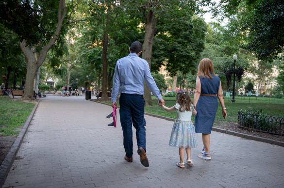 A man, woman, and child walking through a park holding hands