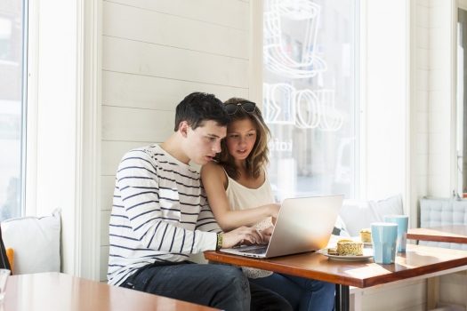 Young couple sitting at table in cafe looking at laptop. 
