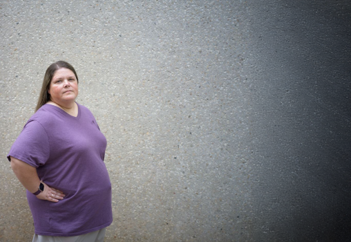 Woman in a purple shirt looking serious standing in front of a wall
