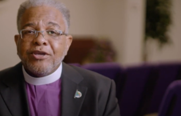 video still of priest being interviewed
